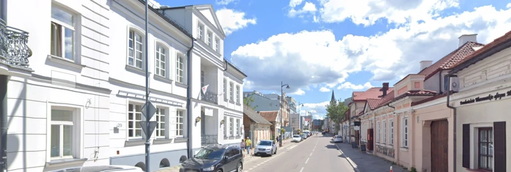 Ulica Warszawska w Białymstoku z historyczną zabudową, kamienicami, lokalami usługowymi i spokojnym ruchem miejskim.