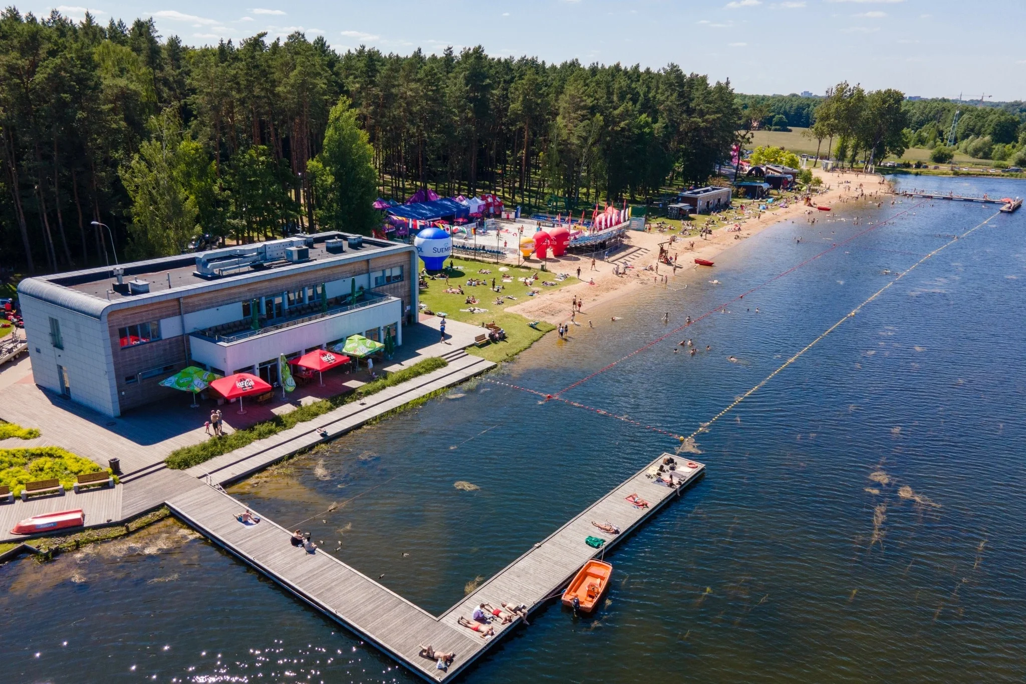 Widok z góry na plażę miejską Dojlidy w Białymstoku, z kąpieliskiem, pomostami, plażowiczami i lasem w tle.