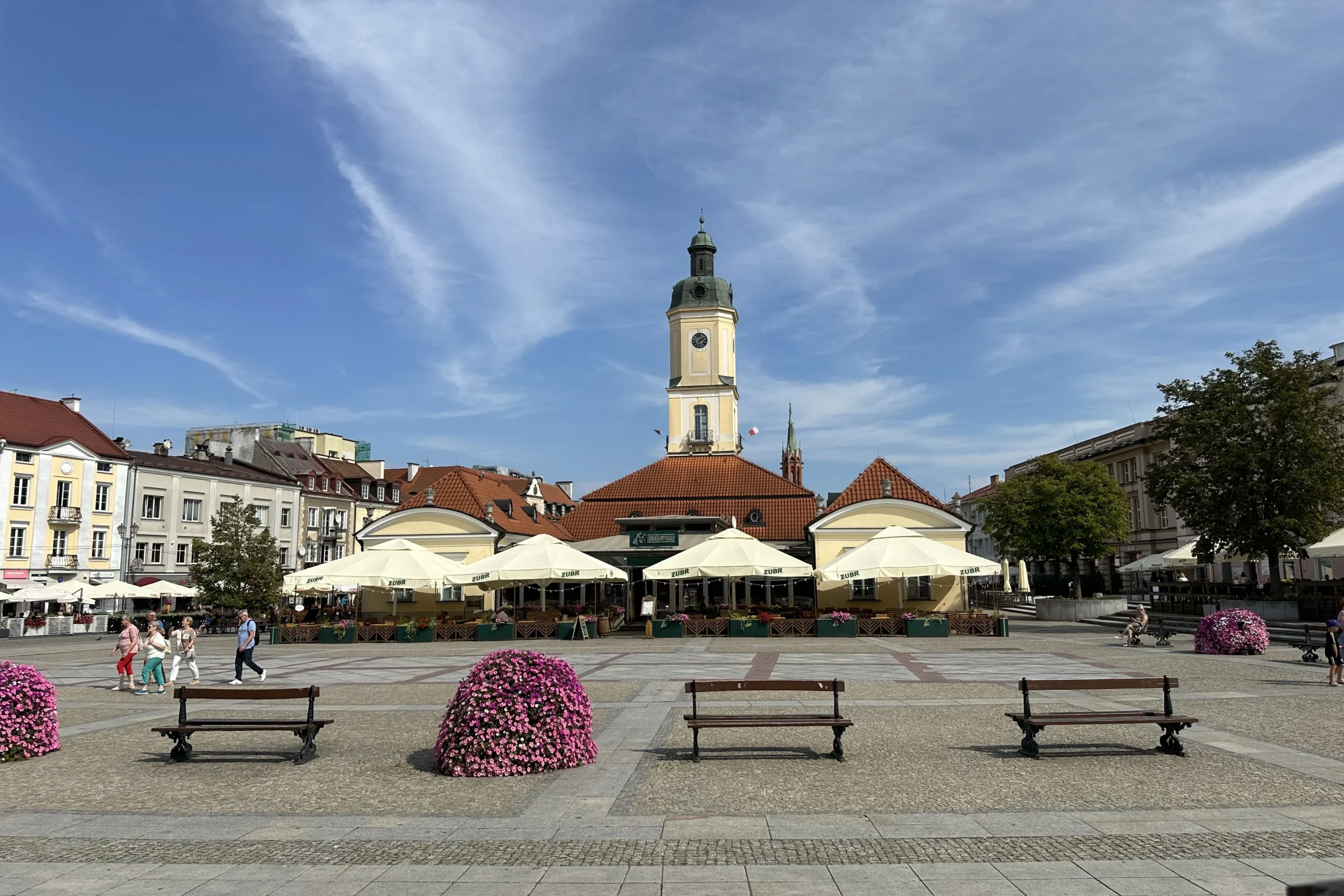 Rynek Kościuszki w Białymstoku z dawnym ratuszem, ogródkami restauracyjnymi, ławkami i spacerującymi mieszkańcami.
