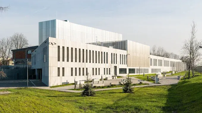 Nowoczesny budynek Muzeum Pamięci Sybiru w Białymstoku z jasną elewacją, pionowymi oknami i zielonym terenem przed wejściem.